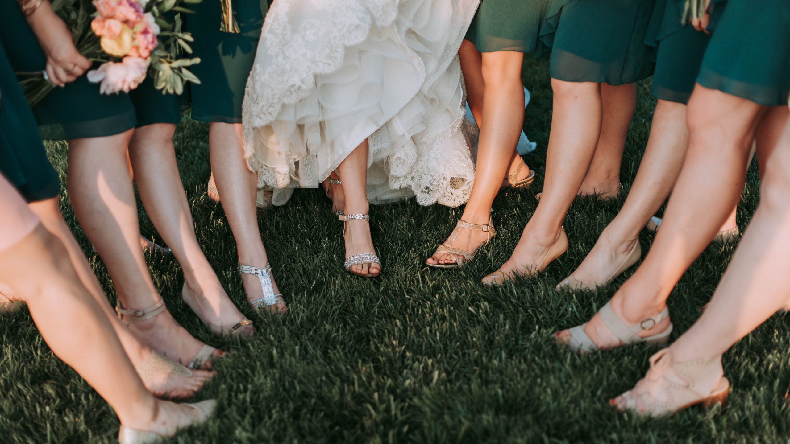 Braut und Brautjungfern stehen auf dem Rasen mit Schuhen