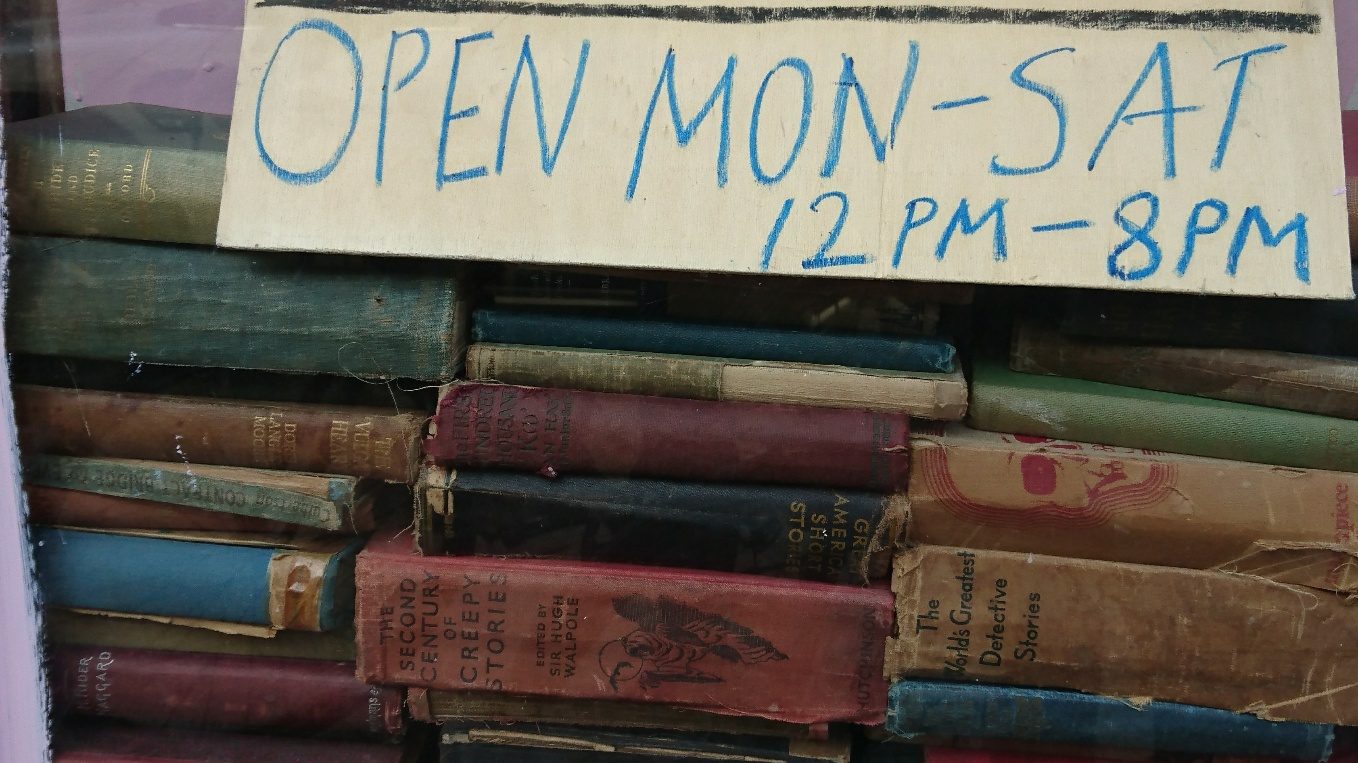 Alte englische Second Hand-Bücher in einem Schaufenster mit selbst geschriebenem Pappschild mit Öffnungszeiten